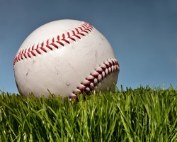 Baseball close up on grass with blue sky behind