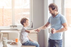 Father and son are giving five and smiling while having a snack in kitchen