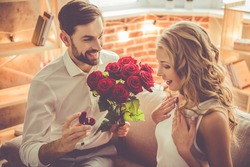 Handsome elegant guy is proposing to his beautiful girlfriend, giving her roses and smiling while they having a romantic date at home