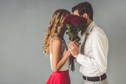 Beautiful elegant couple is kissing behind roses, on gray background