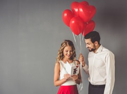 Handsome elegant guy is presenting a gift card and balloons to his beautiful girlfriend and smiling