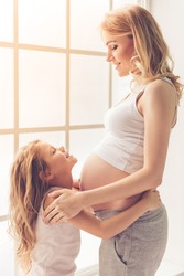 Cute little girl is hugging her beautiful pregnant mom's tummy and smiling