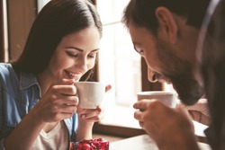 Happy young couple is drinking coffee and smiling while sitting at the cafe