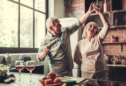 Beautiful senior couple is dancing and smiling while cooking together in kitchen