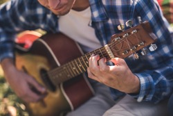 Cropped image of handsome young man playing guitar while resting in the park