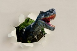 Closeup view of an angry T-Rex dinosaur figurine climbs out of torn paper. Monstrous animal with open mouth and sharp teeth