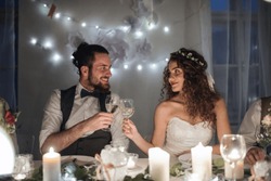 A young couple sitting at a table on a wedding, clinking glasses.