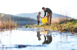 Father with small son collecting rubbish outdoors in nature, plogging concept.