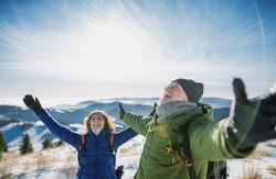 Senior couple hikers in snow-covered winter nature, stretching arms.