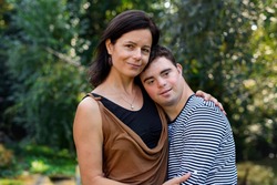 Portrait of down syndrome adult man with mother standing outdoors in garden.