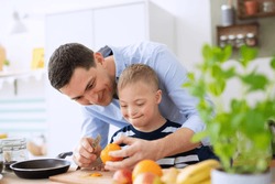 Father with happy down syndrome son indoors in kitchen, preparing food.
