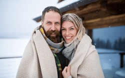 Portrait of happy mature couple in love enjoying holiday in mountain hut, standing outdoors and looking at camera.
