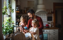 Mature father with two small children washing dishes indoors at home, daily chores concept.