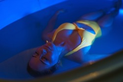 Beautiful woman floating in tank filled with dense salt water used in medical therapy.