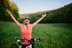 Cheerful active senior woman biker raising arms outdoors in nature.