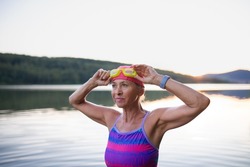 Portrait of active senior woman swimmer outdoors by lake.