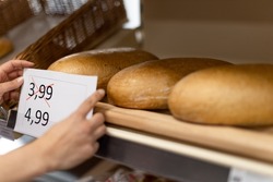 Woman shop assistant changing prices of bread in supermarket, the concept of increasing inflation