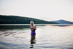 Portrait of active senior woman swimmer standing and splashing outdoors in lake.