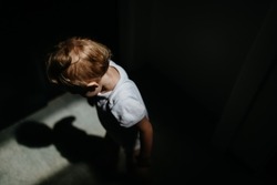 Dark high angle view portrait of sad anonymous little baby girl looking down.