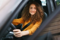 Young woman driving a car in the city. Portrait of a beautiful woman in a car, looking out of the window and smiling.