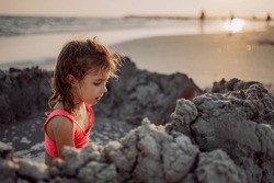 Little girl playing on the beach, digging hole in sand.