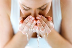 Portrait of beautiful young woman washing her face splashing water in a home bathroom.
