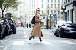 Shot of pretty young woman crossing the street while holding the smartphone and looking sideways.