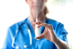 Close-up of female doctor with a spray or nasal drops for the treatment of a runny nose over white background.
