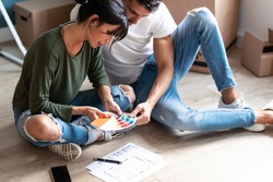 Close up of young attractive couple choosing colors in a color palette to paint the walls of the apartment while sitting on the floor.