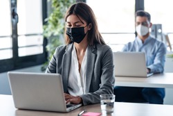 Shot of two attractive business partners wearing a hygienic face mask while working with laptops in the coworking space. Social distancing concept.
