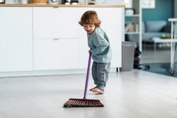 Shot of little cute boy sweeping and cleaning the floor of the kitchen at home.
