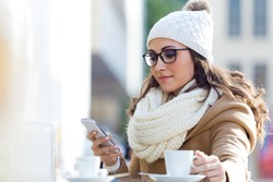Outdoor portrait of young beautiful woman using her mobile phone in a cafe.