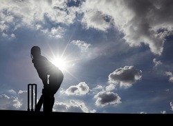 Silhouette of a cricket batter sportsman at the wicket stump on a sunny summer day.