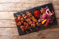 Recipe of a spicy African suya kebab on skewers with fresh vegetable salad and ketchup close-up on a table. horizontal top view from above