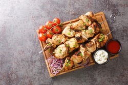 Juicy grilled chicken skewers with fresh vegetables and two sauces close-up on a wooden tray on a gray concrete background. horizontal top view from above