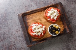 Greek dakos appetizer with barley rusk, tomatoes, feta cheese, oregano and olive oil closeup on the wooden board on the table. Horizontal top view from above