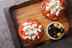 Cretan dakos is for a traditional salad from the island of Crete consists of barley rusk topped with juicy tomatoes, cheese and olive oil closeup on the wooden board. Horizontal top view