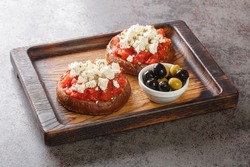 Greek dakos appetizer with barley rusk, tomatoes, feta cheese, oregano and olive oil closeup on the wooden board on the table. Horizontal