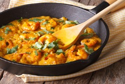 Prawns in curry sauce in a black frying pan close-up. Horizontal 