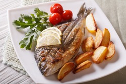 Grilled dorado fish with fried potatoes and lemon on a plate close-up. Horizontal
