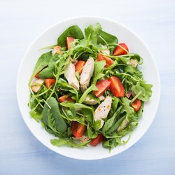 Fresh salad with chicken, tomato and greens (spinach, arugula) on blue wooden background top view. Healthy food.