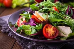 Fresh salad with chicken, tomatoes and mixed greens (arugula, mesclun, mache) on wooden background close up. Healthy food.