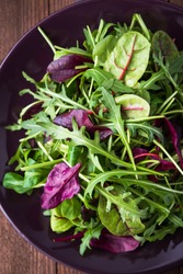 Fresh salad with mixed greens (arugula, mesclun, mache) on dark wooden background top view. Healthy food.