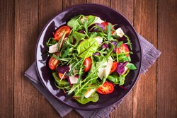 Fresh salad with chicken, tomatoes and mixed greens (arugula, mesclun, mache) on wooden background top view. Healthy food. Meat and vegetables.