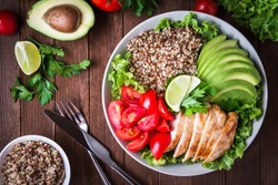 Healthy salad plate with quinoa, cherry tomatoes, chicken, avocado, lime and mixed greens, lettuce, parsley on wooden background top view. Food and health. Superfood meal.