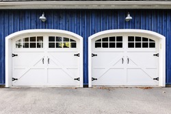 Two white garage doors with windows on blue house