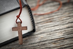 Closeup of wooden Christian cross necklace next to holy Bible