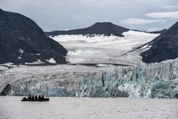 arctic glacier and icebergs off coast of norwegian svalbard islands, with exploration boat of adventurers viewing.