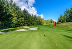 Golf course with gorgeous green, sand bunker and golf flag and real estate on background.