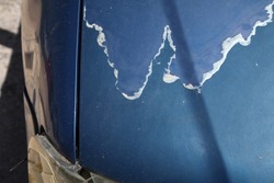Weathered car hood paint coat. Peeling sun damaged paint surface in a 15 year old compact blue car.